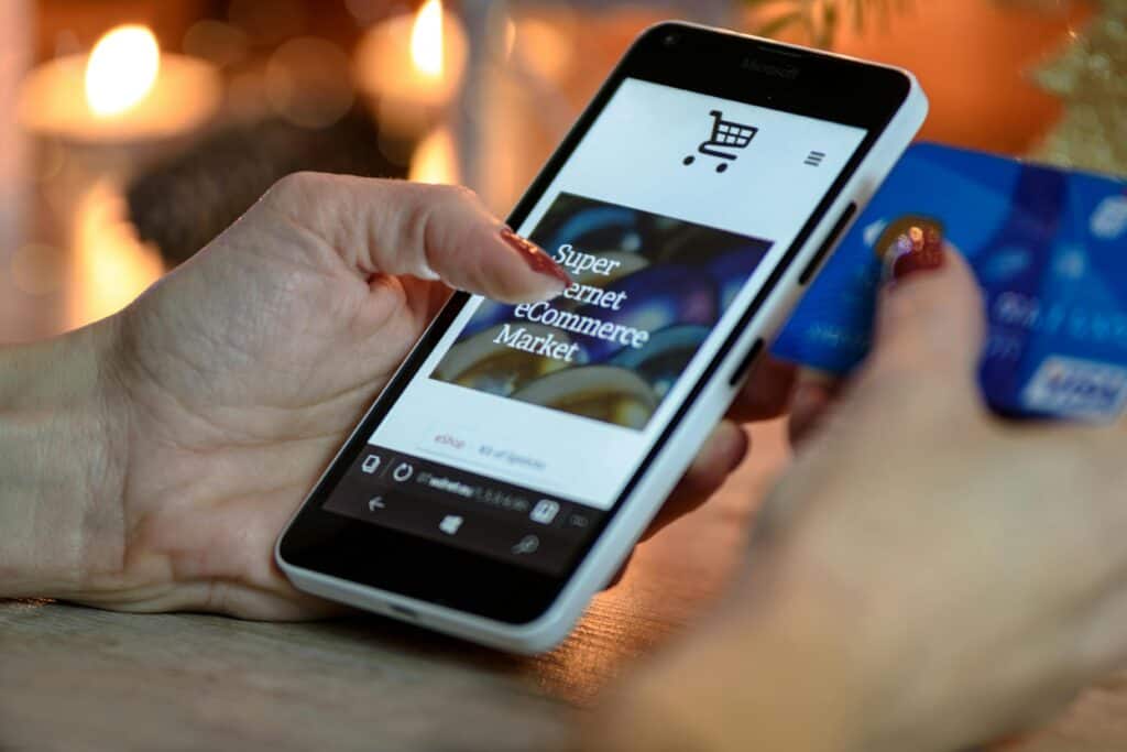 pexels-photo-230544-230544 Woman using smartphone for online shopping with credit card in hand, festive background lighting.